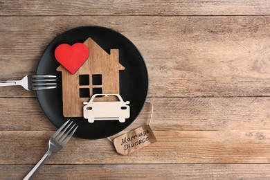Divorce concept. Plate with model of house, car, heart and forks near paper card on wooden table, flat lay. Space for text