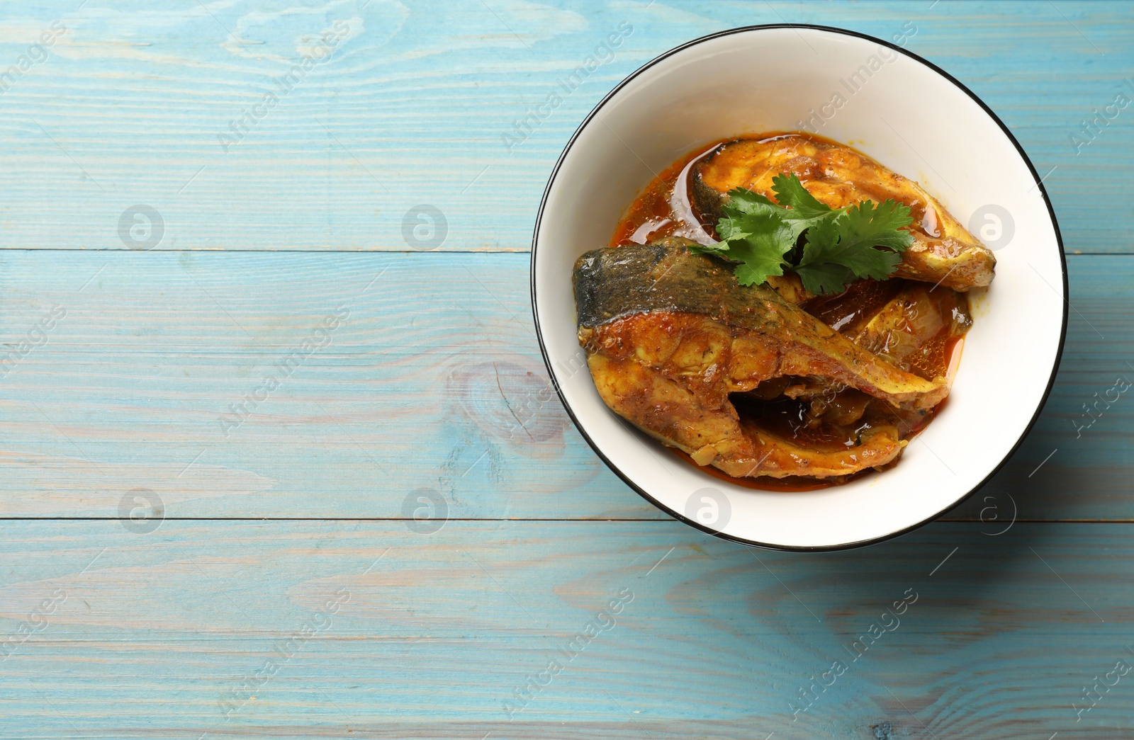 Photo of Tasty fish curry on light blue wooden table, top view. Space for text. Indian cuisine