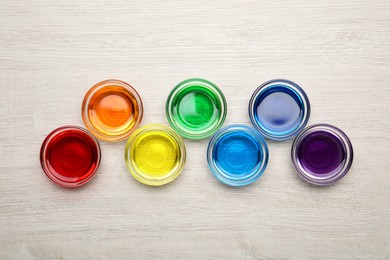 Glass bowls with different food coloring on wooden table, flat lay