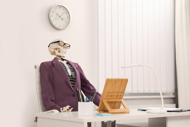 Photo of Human skeleton in suit at table in office
