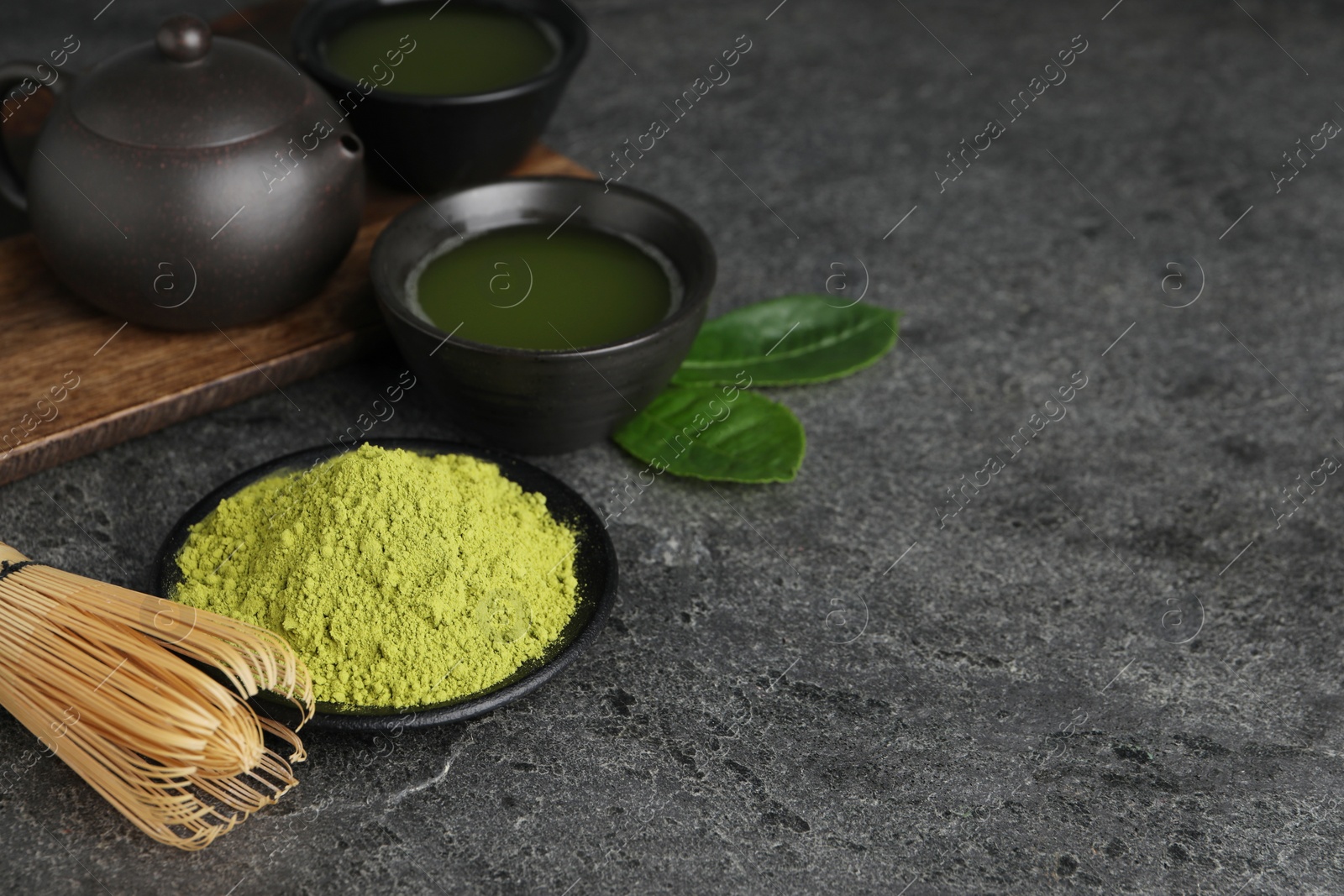 Photo of Green matcha powder, bamboo whisk and fresh beverage on grey table. Space for text