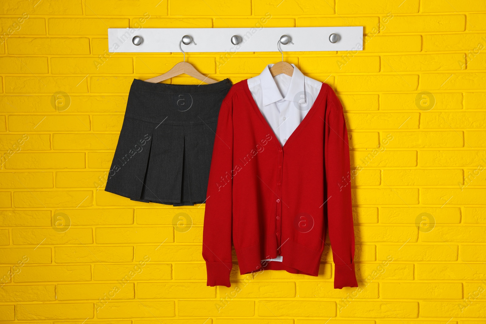 Photo of Shirt, jumper and skirt hanging on yellow brick wall. School uniform