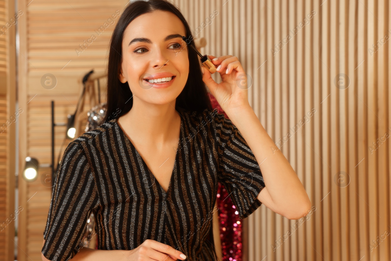 Photo of Beautiful young woman applying mascara in dressing room