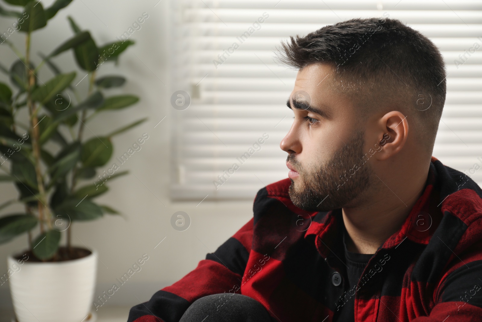 Photo of Sad young man at home. Space for text