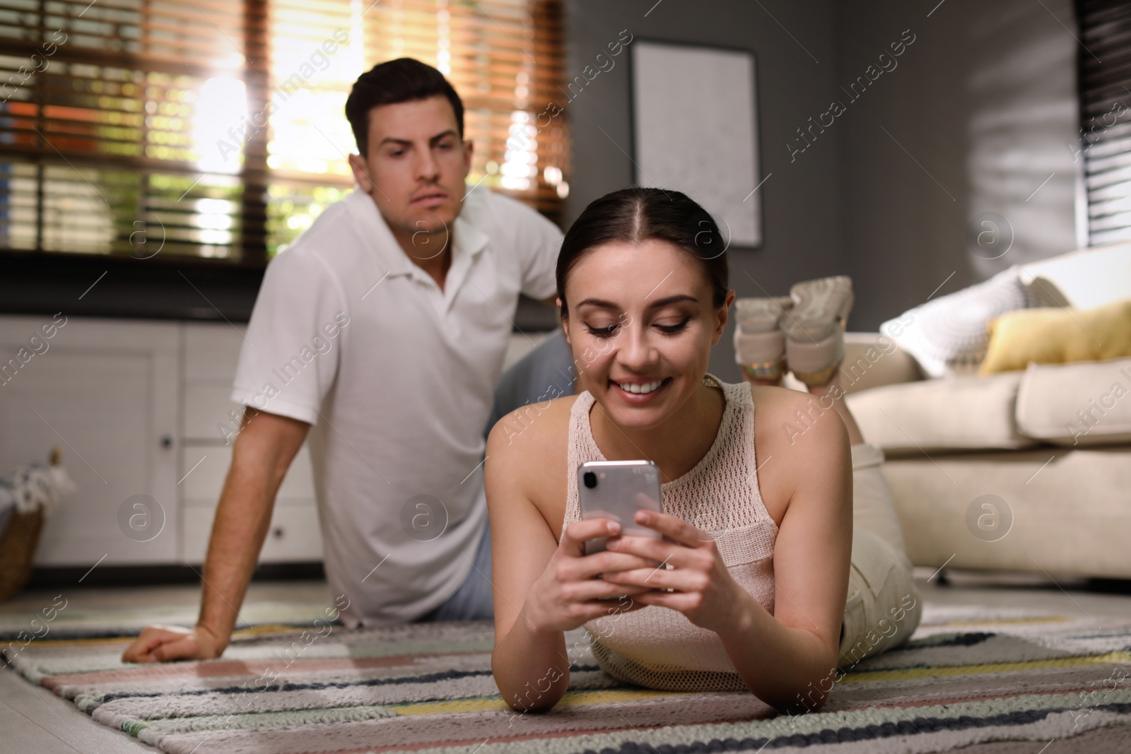 Photo of Distrustful man peering into girlfriend's smartphone at home. Jealousy in relationship