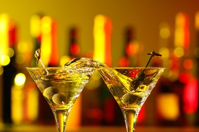 Photo of Clinking martini glasses with splashing cocktail and olives in bar, closeup
