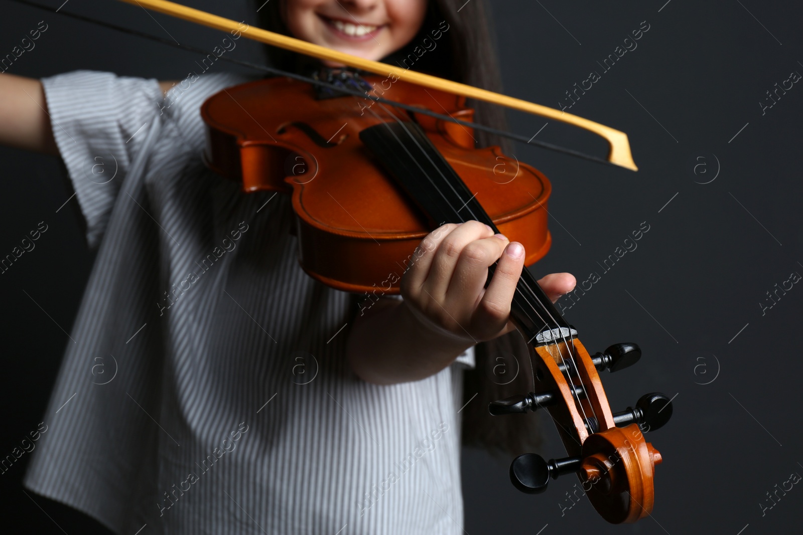 Photo of Preteen girl playing violin on black background, closeup