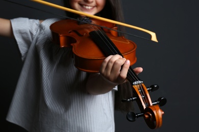 Preteen girl playing violin on black background, closeup