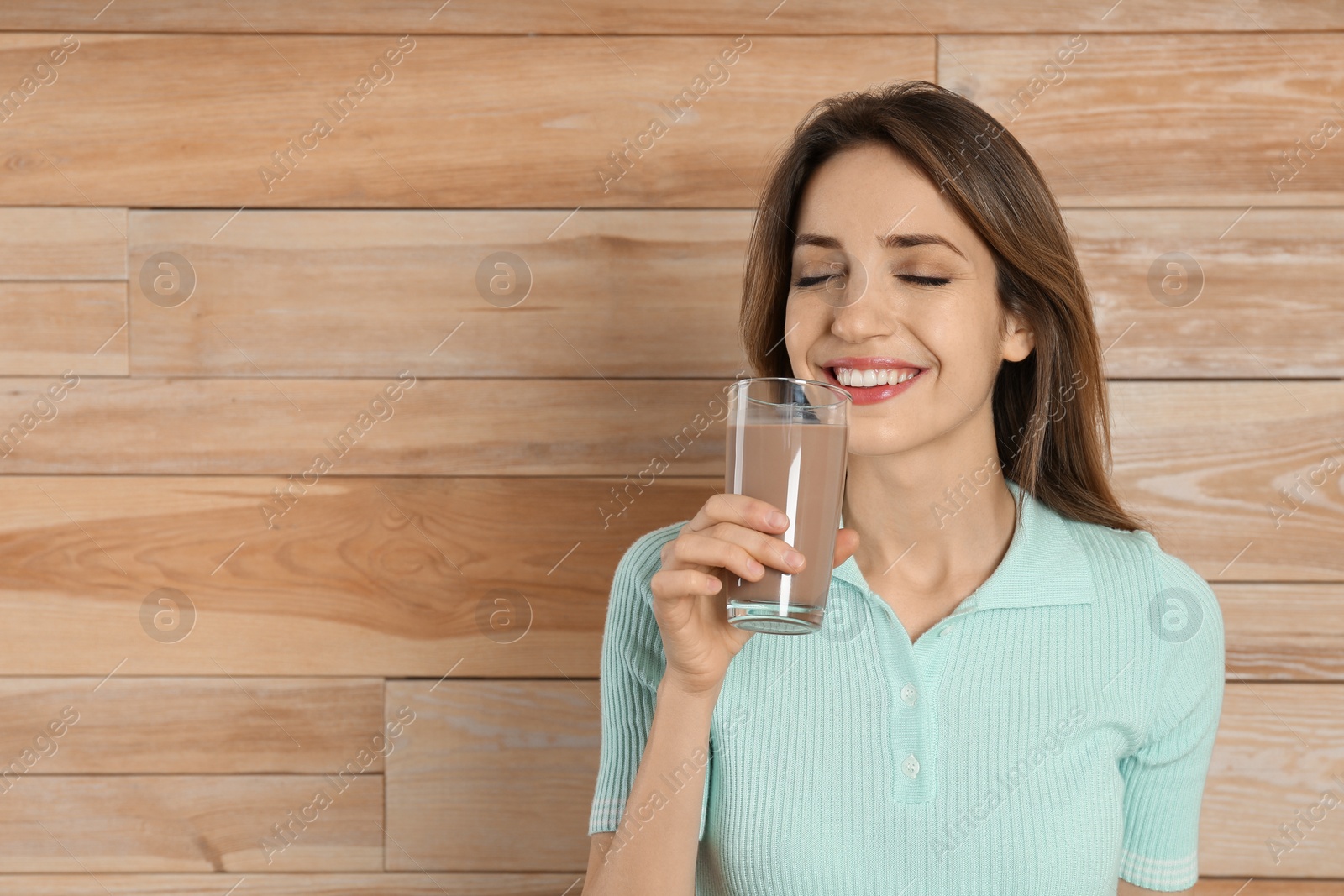 Photo of Young woman drinking chocolate milk on wooden background. Space for text