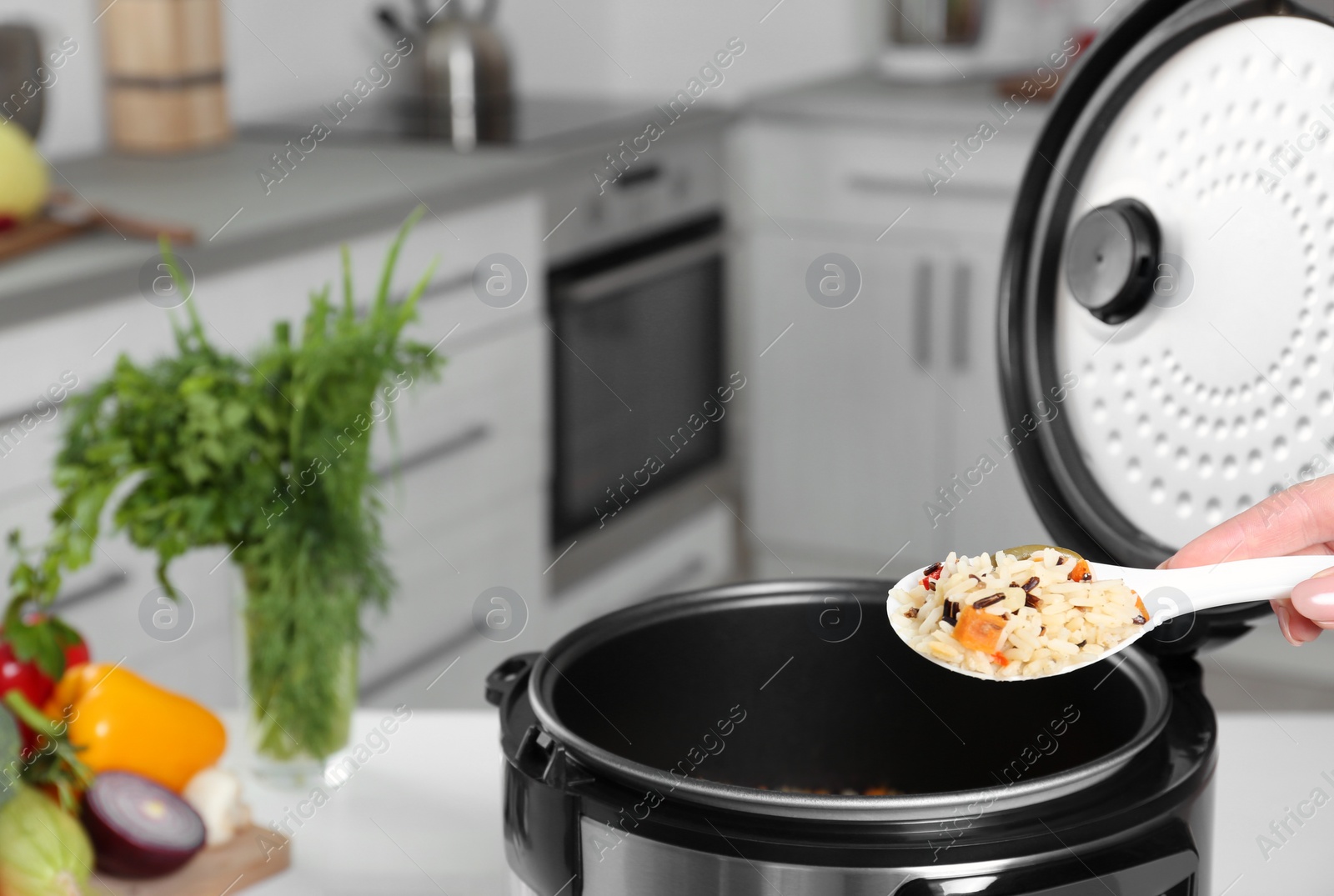 Photo of Woman holding spoon with prepared rice over multi cooker, closeup. Space for text