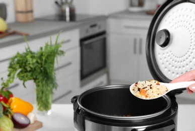 Woman holding spoon with prepared rice over multi cooker, closeup. Space for text