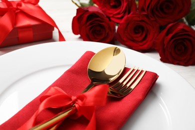 Beautiful dishware with gift and bouquet on white wooden table, closeup. Romantic date