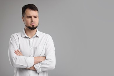 Portrait of sad man with crossed arms on grey background, space for text