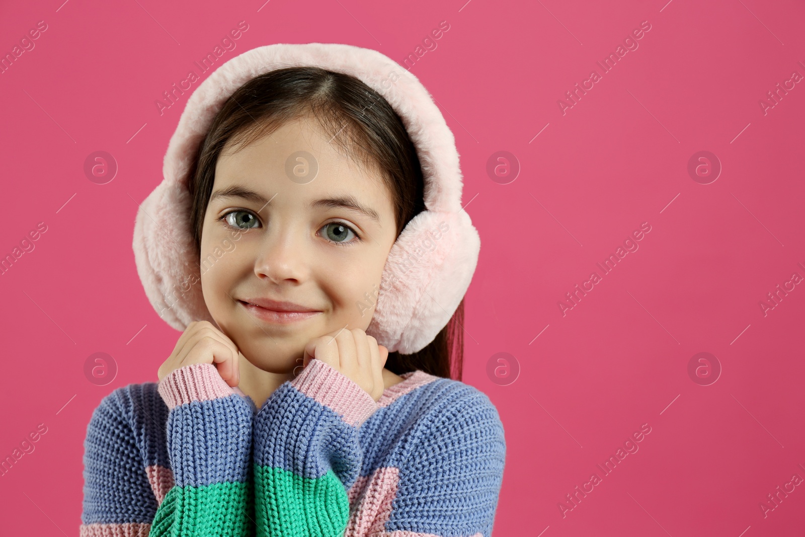 Photo of Cute little girl wearing stylish earmuffs on pink background. Space for text