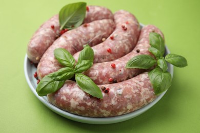 Photo of Raw homemade sausages, basil leaves and peppercorns on green table, closeup