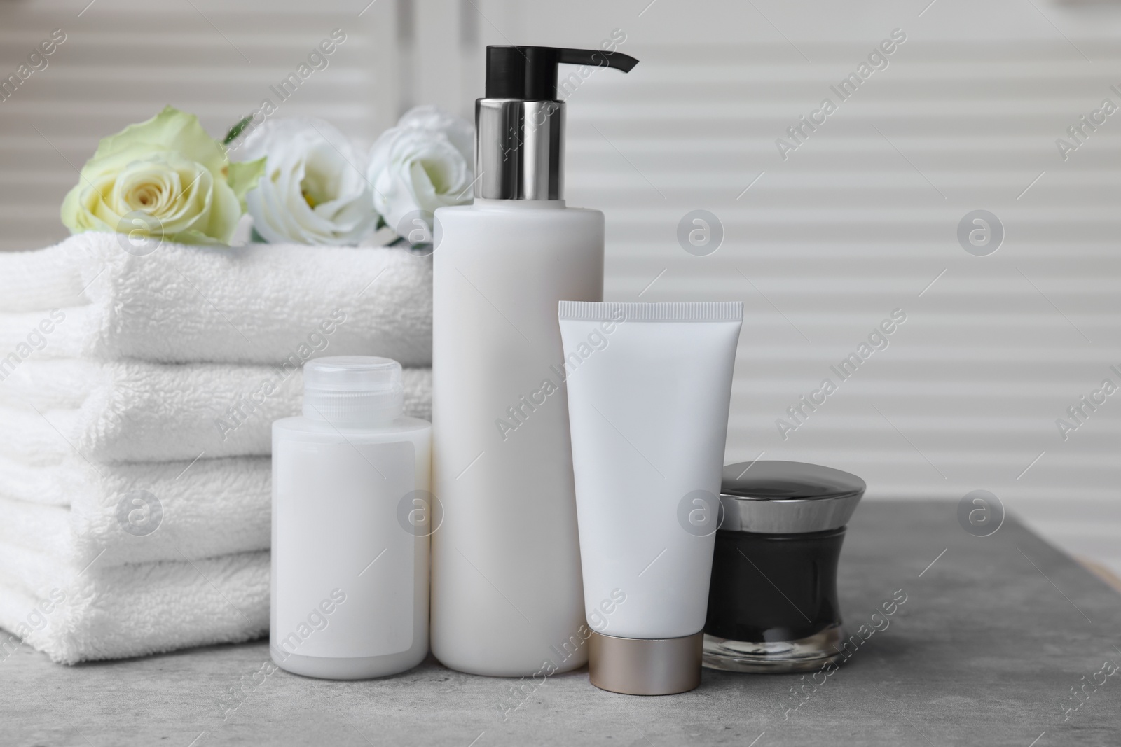 Photo of Towels, cosmetic products and flowers on grey table indoors