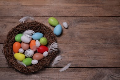 Flat lay composition with festively decorated Easter eggs and feathers on wooden table. Space for text