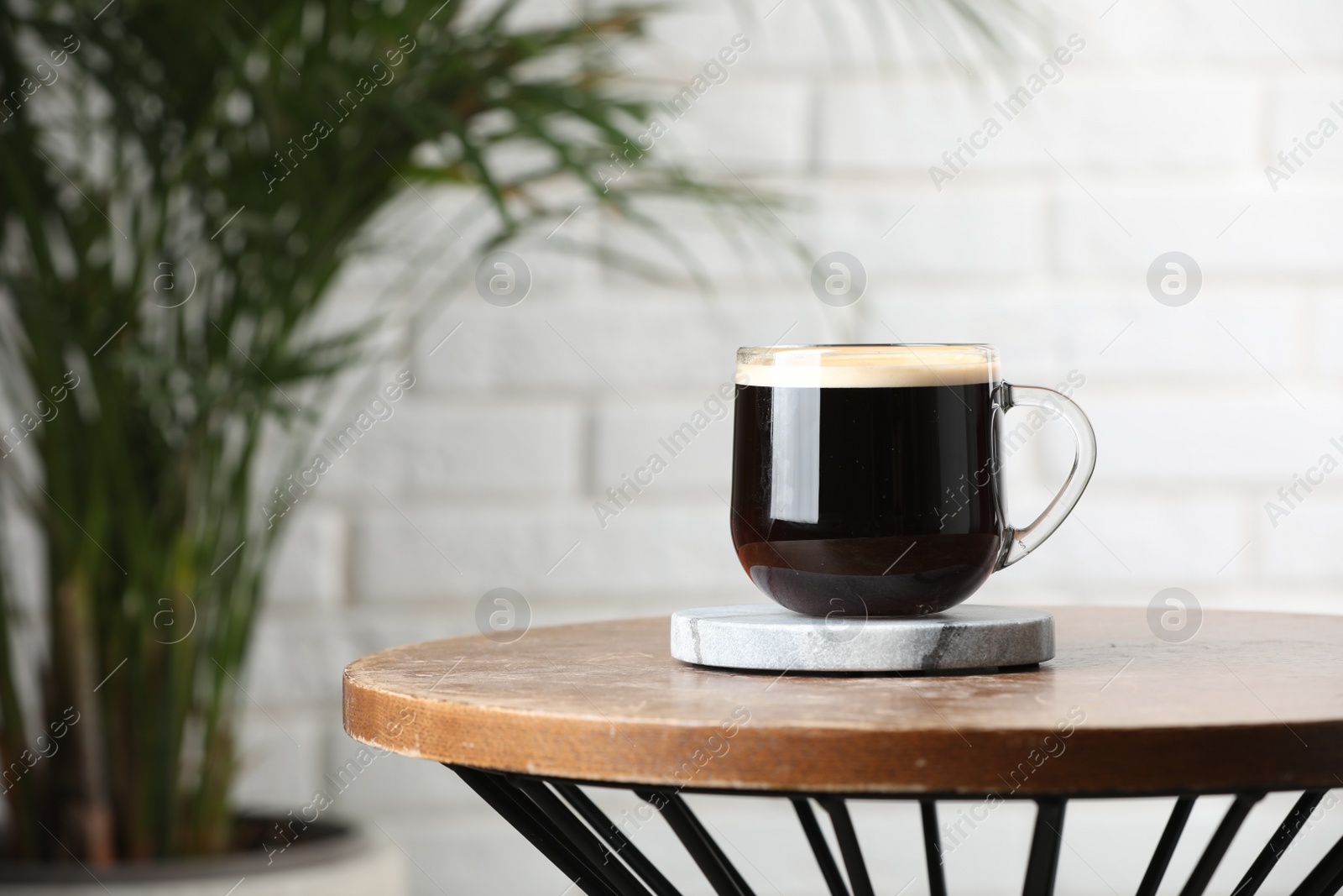 Photo of Glass mug of coffee with stylish stone cup coaster on wooden table in room. Space for text