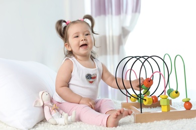 Photo of Adorable little baby girl playing with bead maze on bed in room