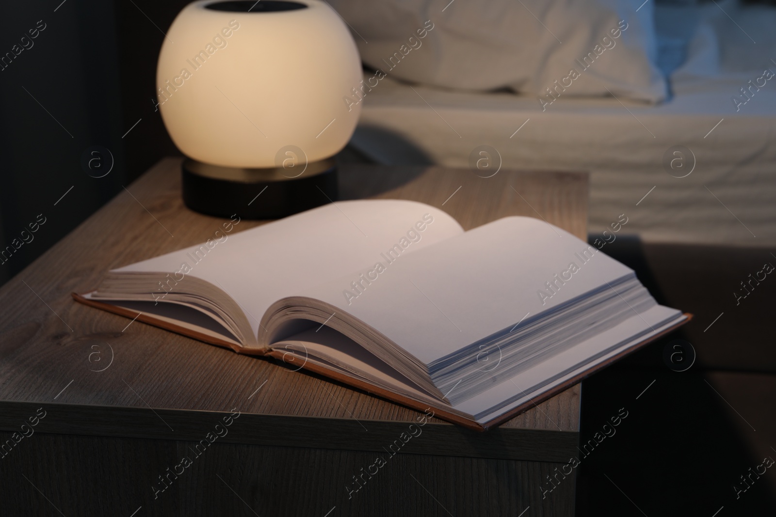 Photo of Stylish nightlight and book on bedside table near bed indoors