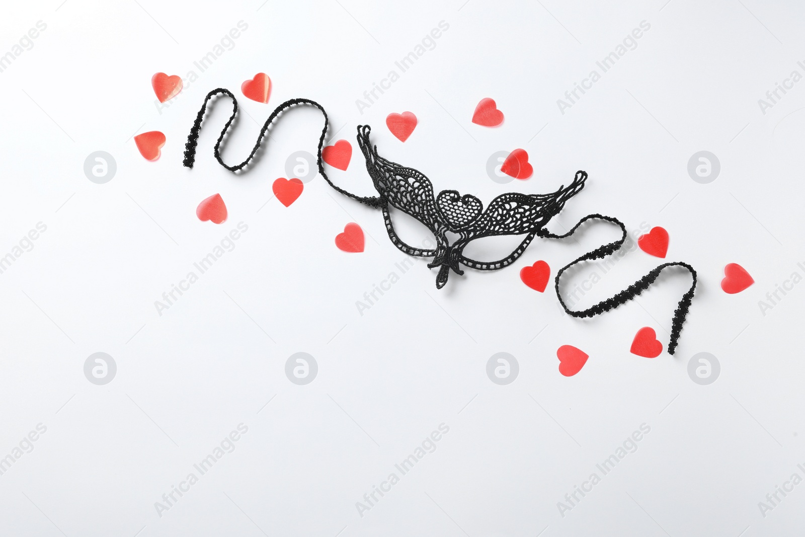 Photo of Black lace mask for sexual role play and red hearts on white background