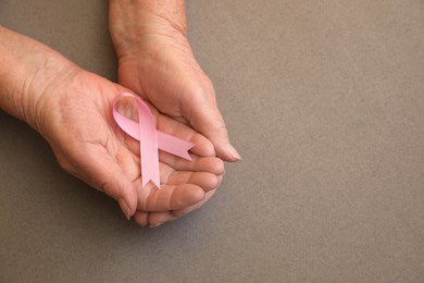 Photo of Senior woman holding pink ribbon on grey background, top view with space for text. Breast cancer awareness