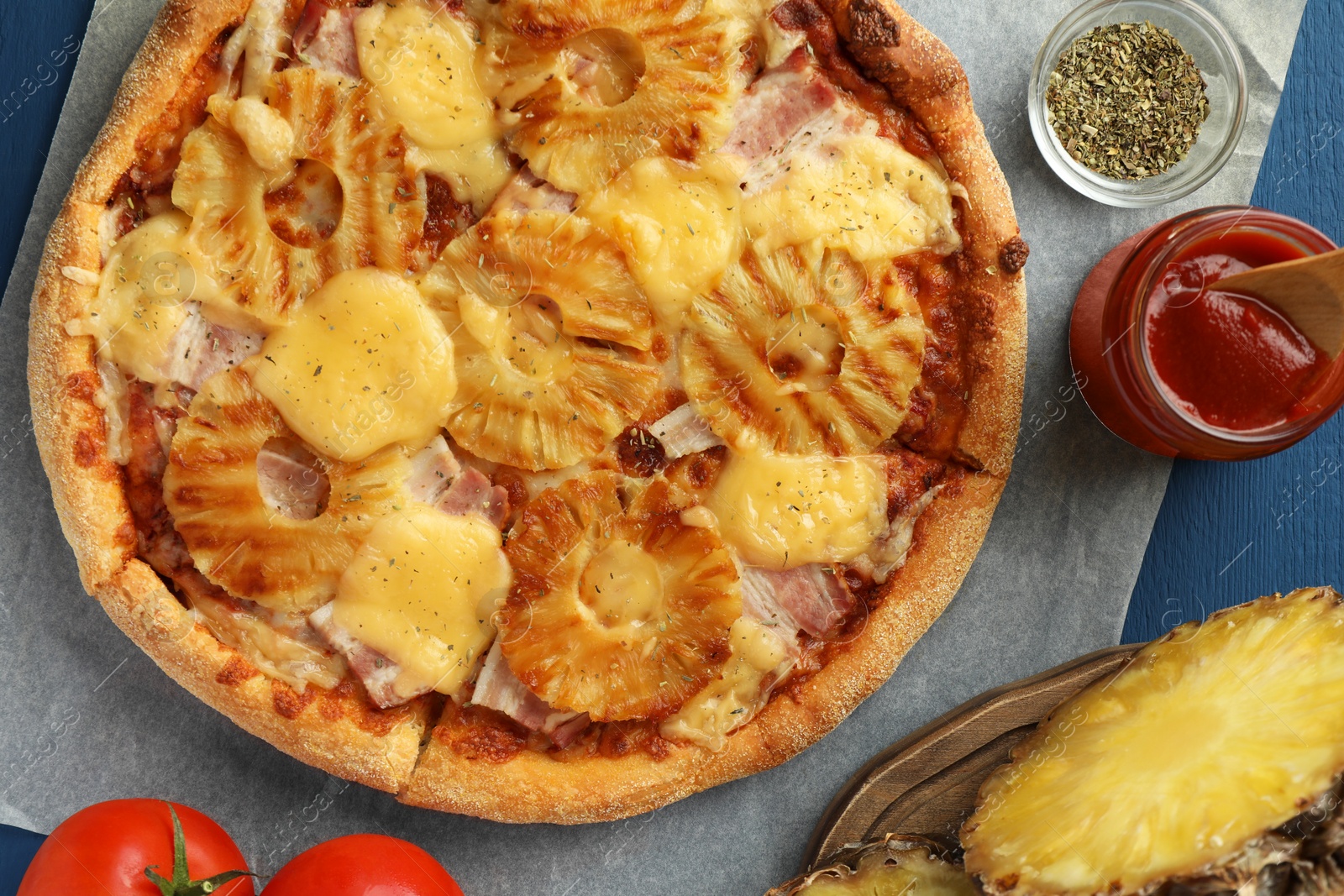 Photo of Delicious pineapple pizza and ingredients on blue table, flat lay