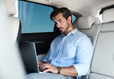Photo of Attractive young man working with laptop on backseat in luxury car