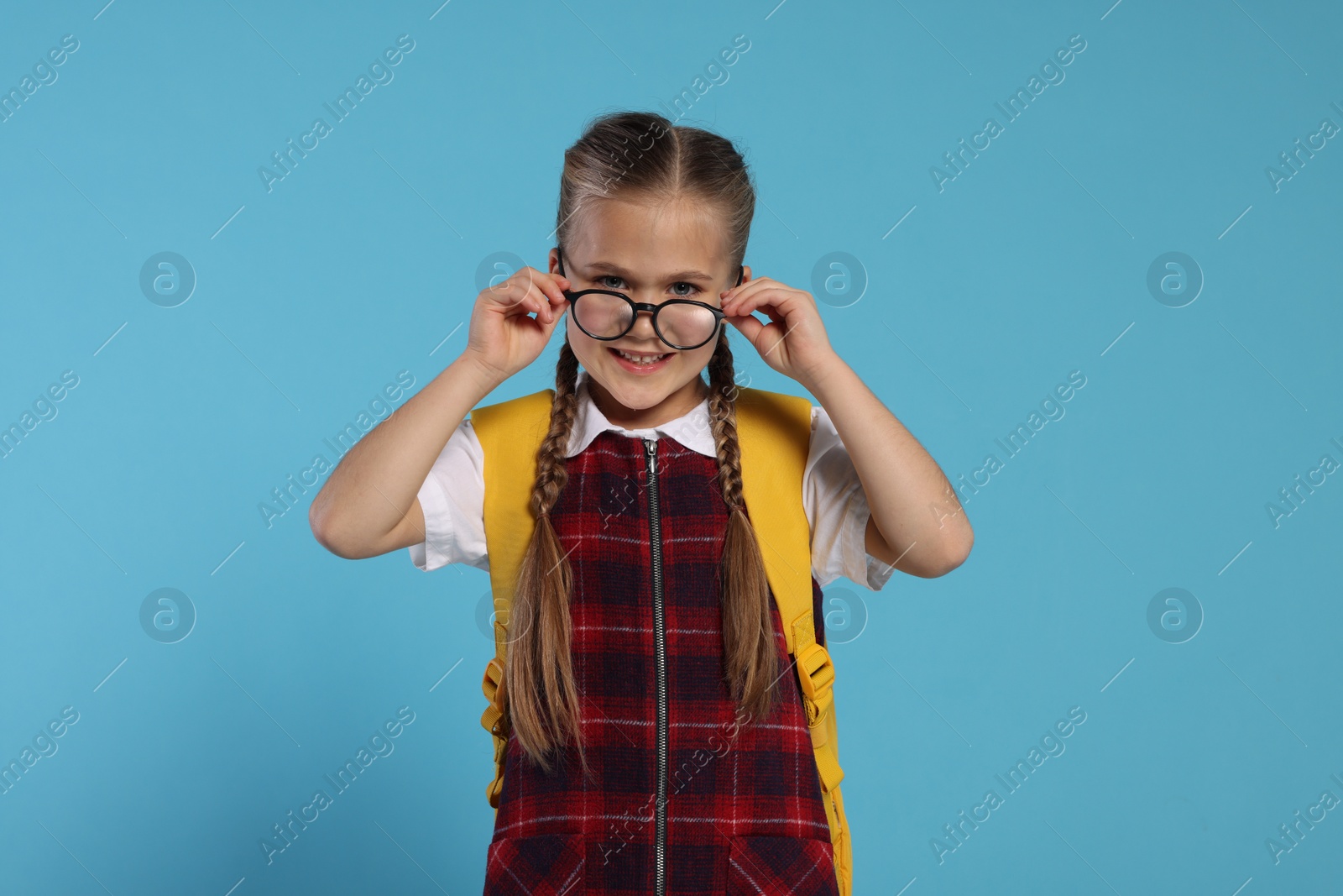 Photo of Happy schoolgirl in glasses with backpack on light blue background