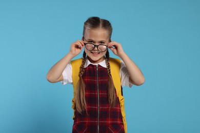 Photo of Happy schoolgirl in glasses with backpack on light blue background