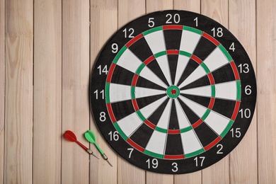 Photo of Dart board with color arrows on wooden background, top view. Space for text