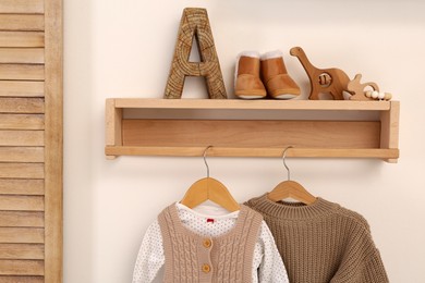 Wooden shelf with baby clothes and toys on white wall indoors