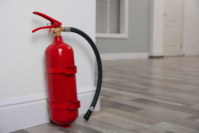 Photo of Fire extinguisher near white wall indoors. Space for text