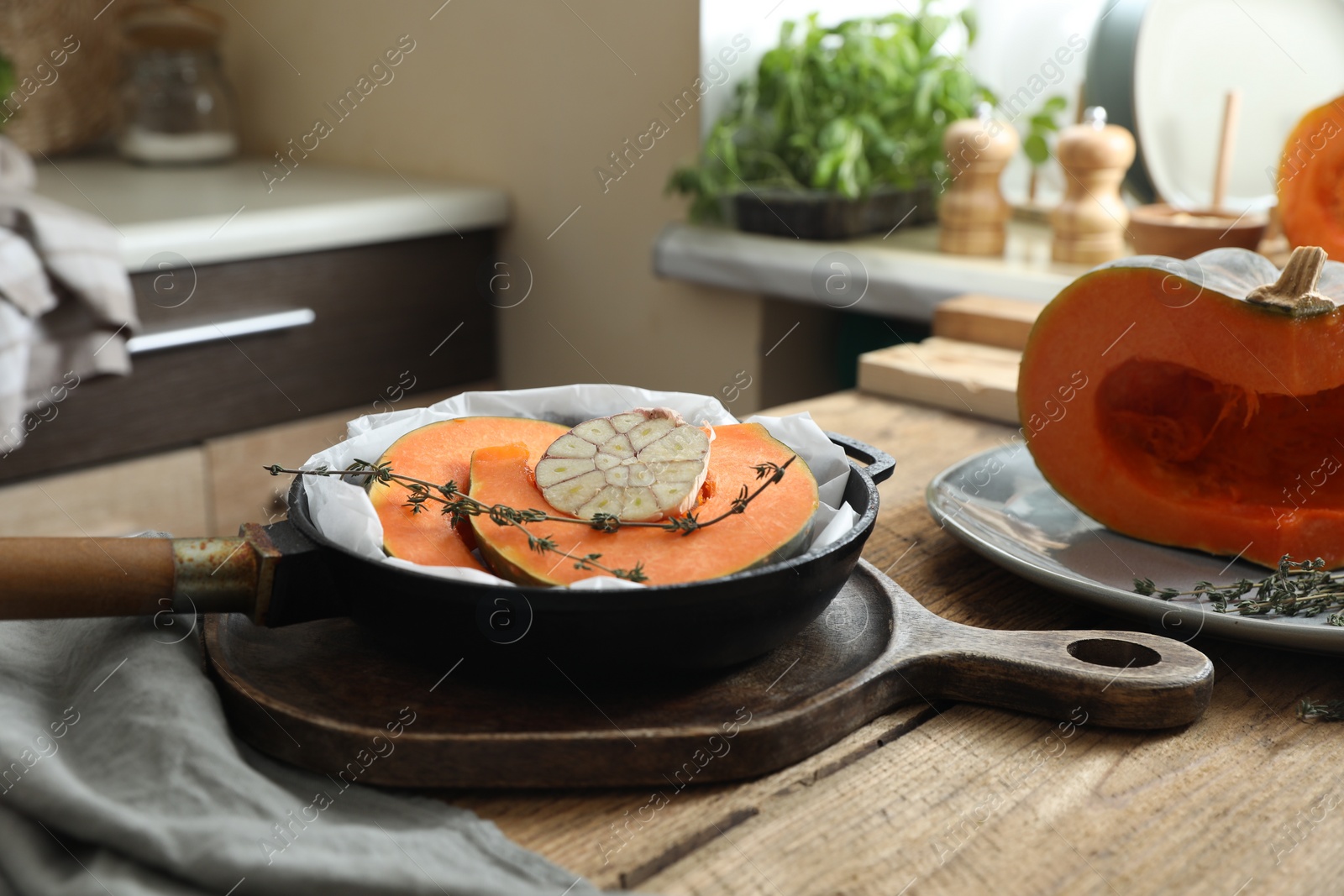 Photo of Fresh pumpkin slices with aromatic thyme and garlic in frying pan on wooden table in kitchen