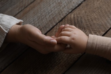 Photo of Woman holding hands with her granddaughter at wooden table, closeup