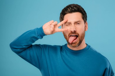 Photo of Man showing his tongue and V-sign on light blue background