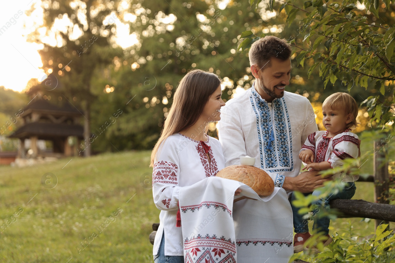 Photo of Happy cute family in embroidered Ukrainian shirts with korovai bread near rustic fence outdoors. Space for text