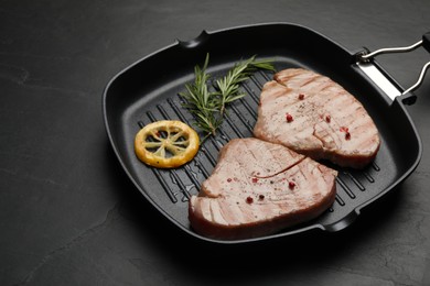 Photo of Delicious tuna steaks with lemon and rosemary on black table