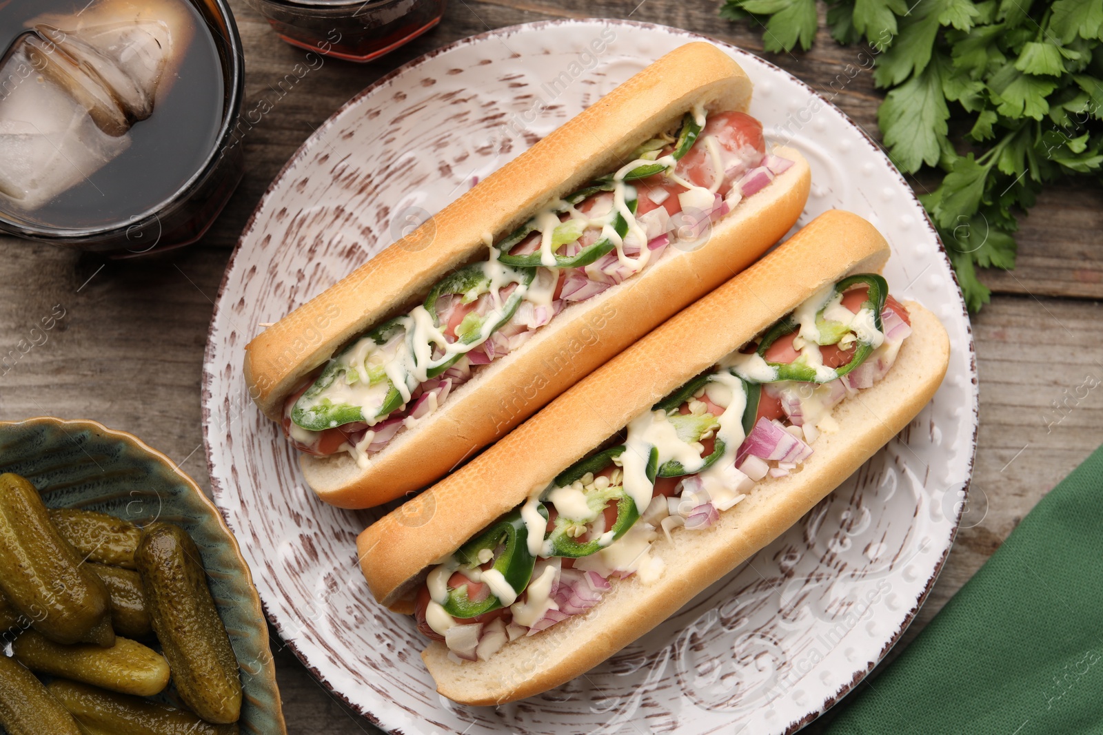 Photo of Delicious hot dogs with onion, chili pepper and sauce served on wooden table, flat lay