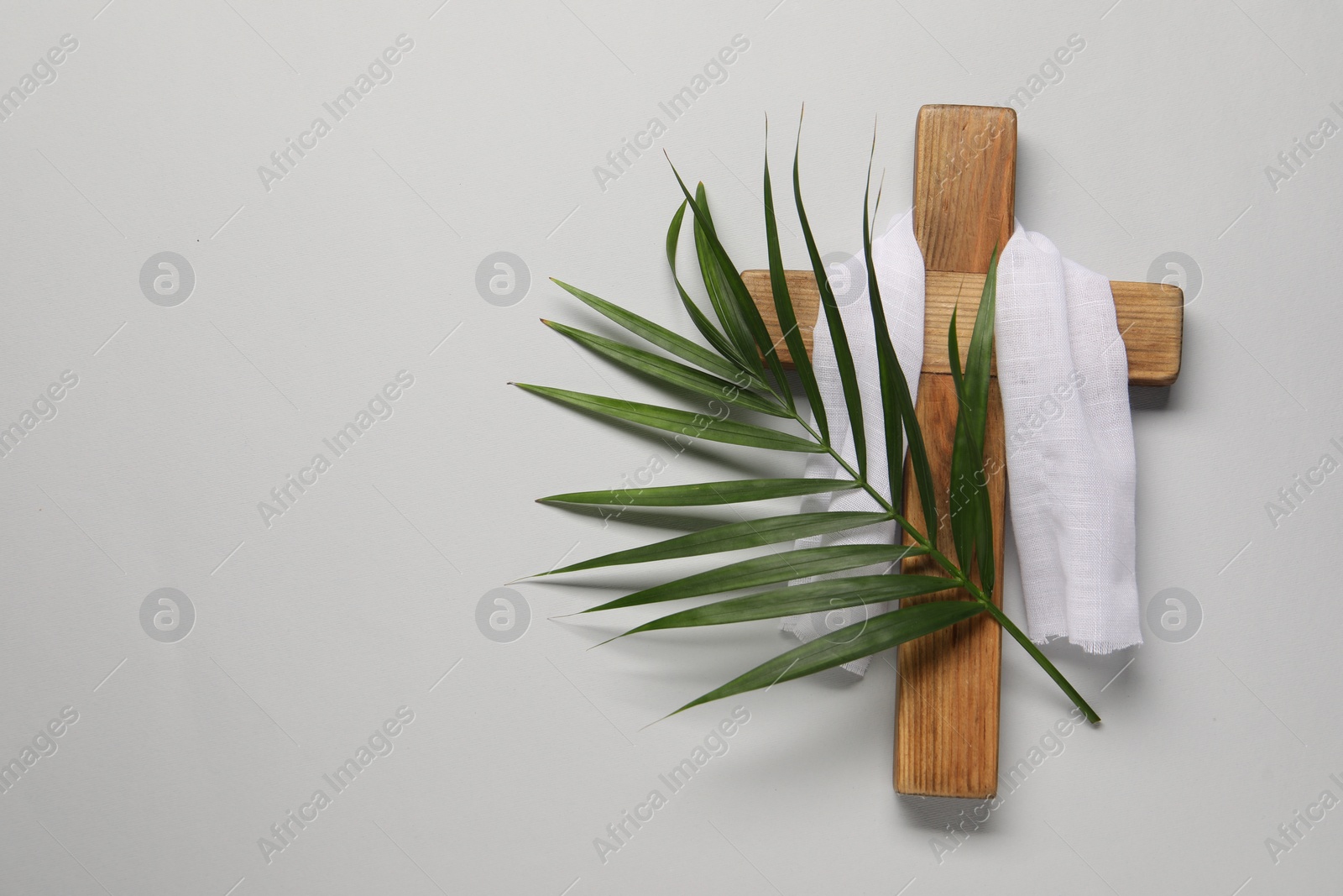 Photo of Wooden cross, white cloth and palm leaf on light grey background, top view with space for text. Easter attributes