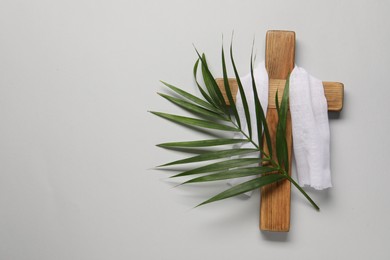 Wooden cross, white cloth and palm leaf on light grey background, top view with space for text. Easter attributes