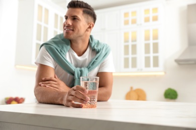 Photo of Man holding glass of pure water at table in kitchen, focus on hand