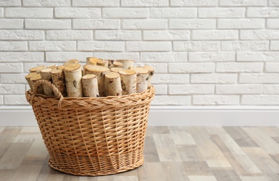 Wicker basket with firewood near white brick wall indoors, space for text