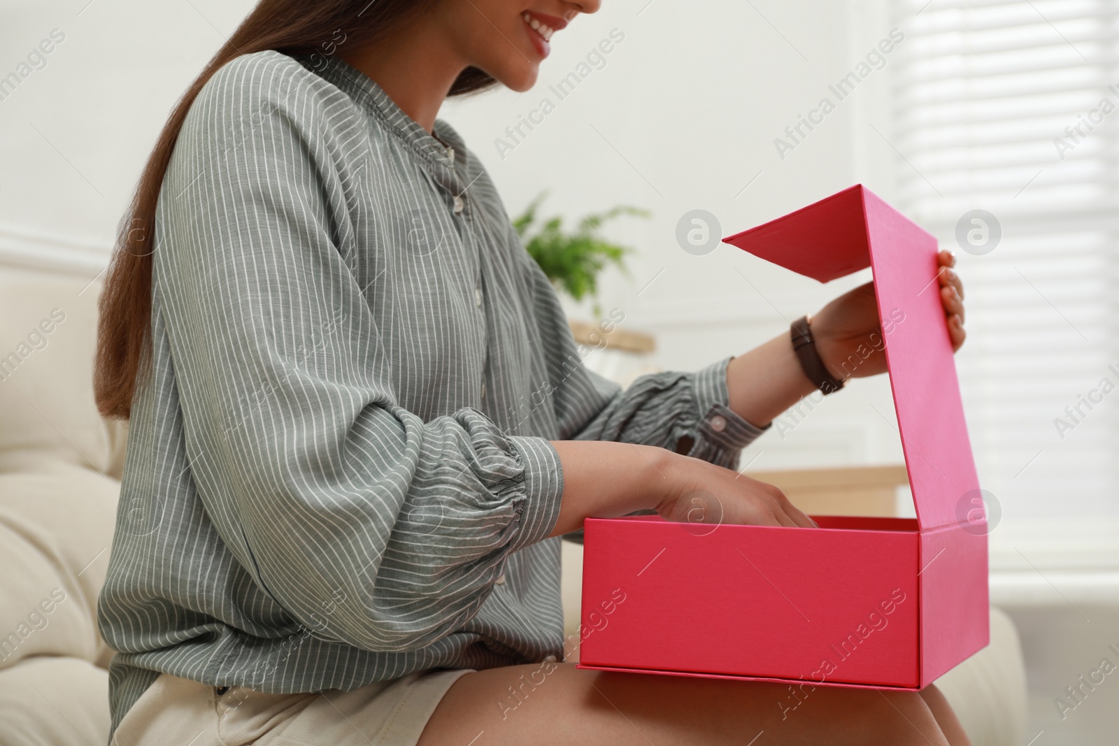 Photo of Happy young woman opening parcel at home, closeup. Internet shopping