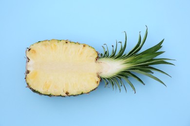 Photo of Half of ripe pineapple on light blue background, top view