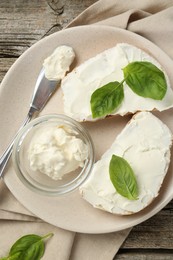 Photo of Delicious sandwiches with cream cheese and basil leaves on wooden table, top view