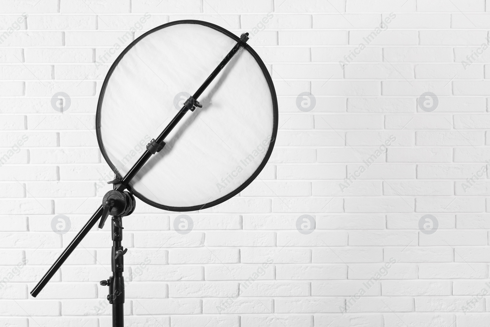 Photo of Professional light reflector on tripod against white brick wall, space for text. Photography equipment