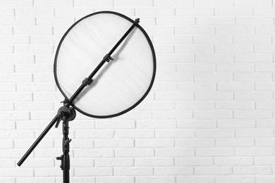 Photo of Professional light reflector on tripod against white brick wall, space for text. Photography equipment