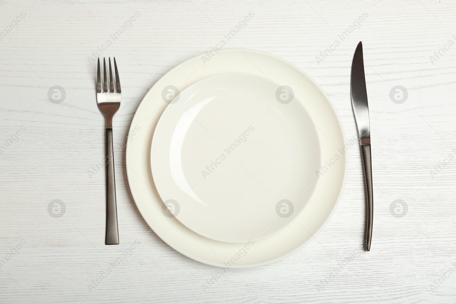 Photo of Empty dishware and cutlery on light wooden background, top view. Table setting