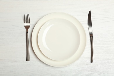Photo of Empty dishware and cutlery on light wooden background, top view. Table setting